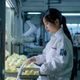 瓜瓜基地品控总监林晓霜，女性，穿白色实验服在检测室内查看瓜果样本，画面专业严谨